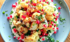 An above shot of roasted cauliflower florets topped with pomegranate and chopped fresh coriander. This is sitting on a bed of tahini sauace.