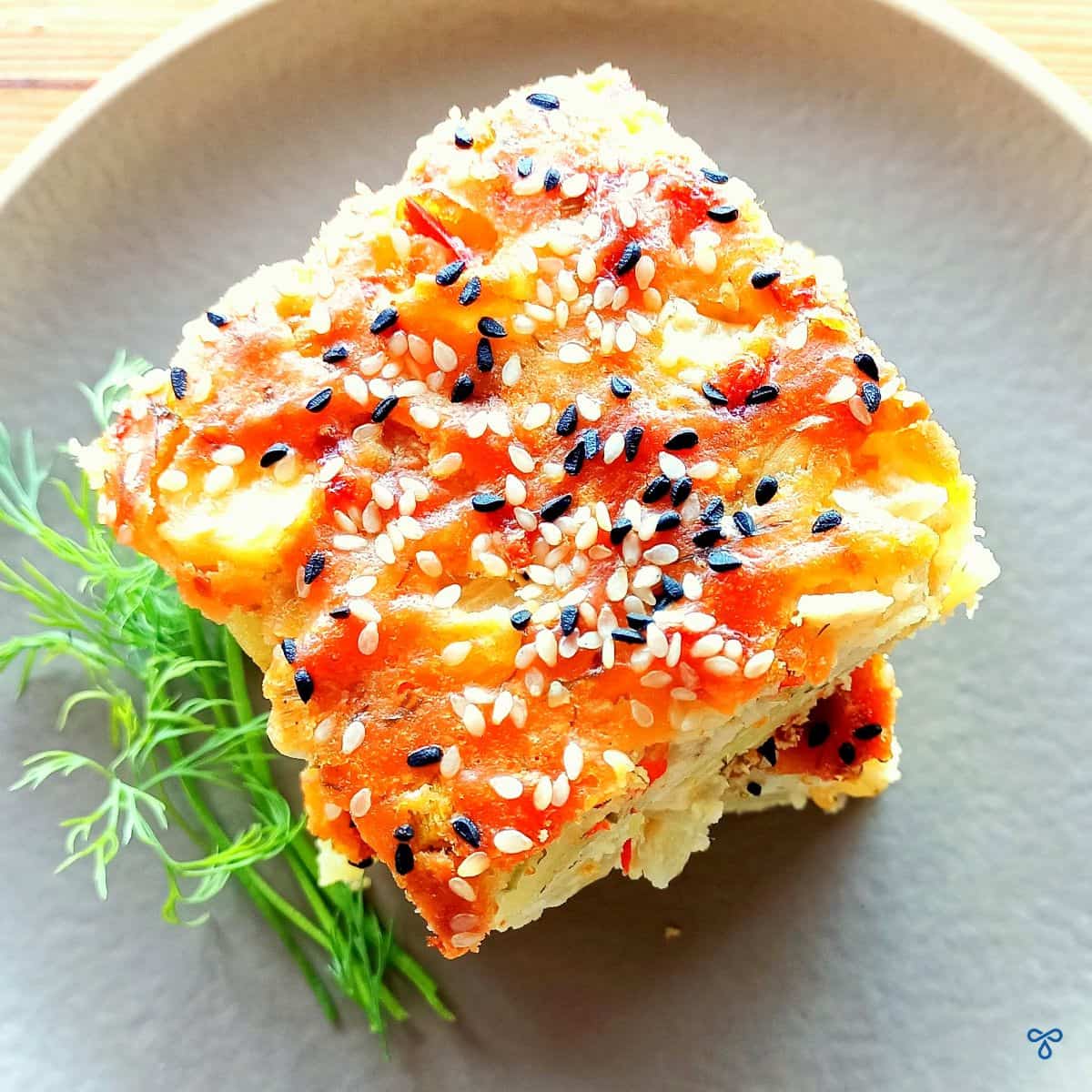 A slice of Turkish potato cake taken from above. The top is golden brown and sprinkled with nigella seeds and sesame seeds.