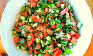 A bowl of finely chopped salad taken from above. Peppers, tomatoes, onion and cucumber are visible.